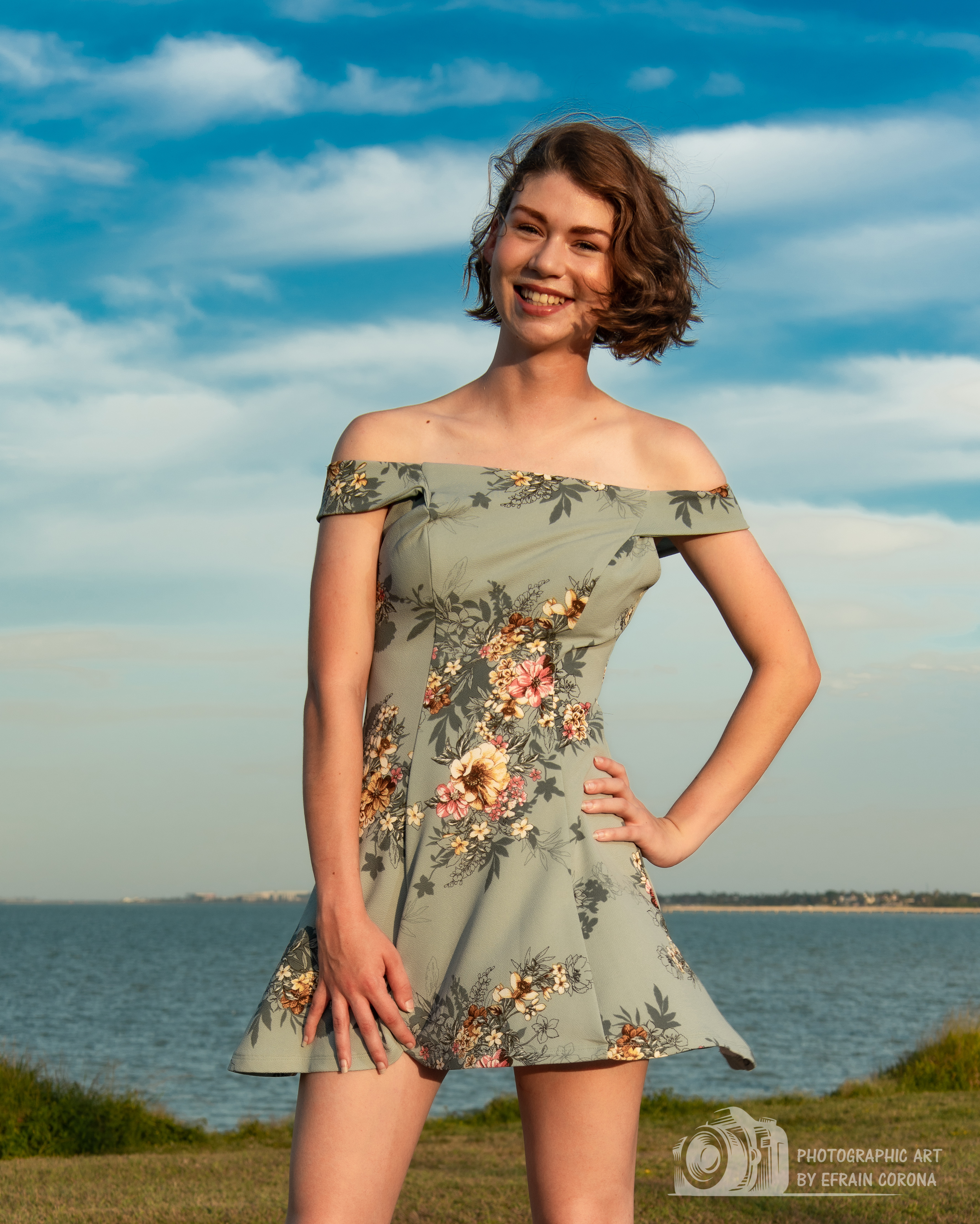 Hailey posing by the ocean in an off-the-shoulder, blue floral dress.