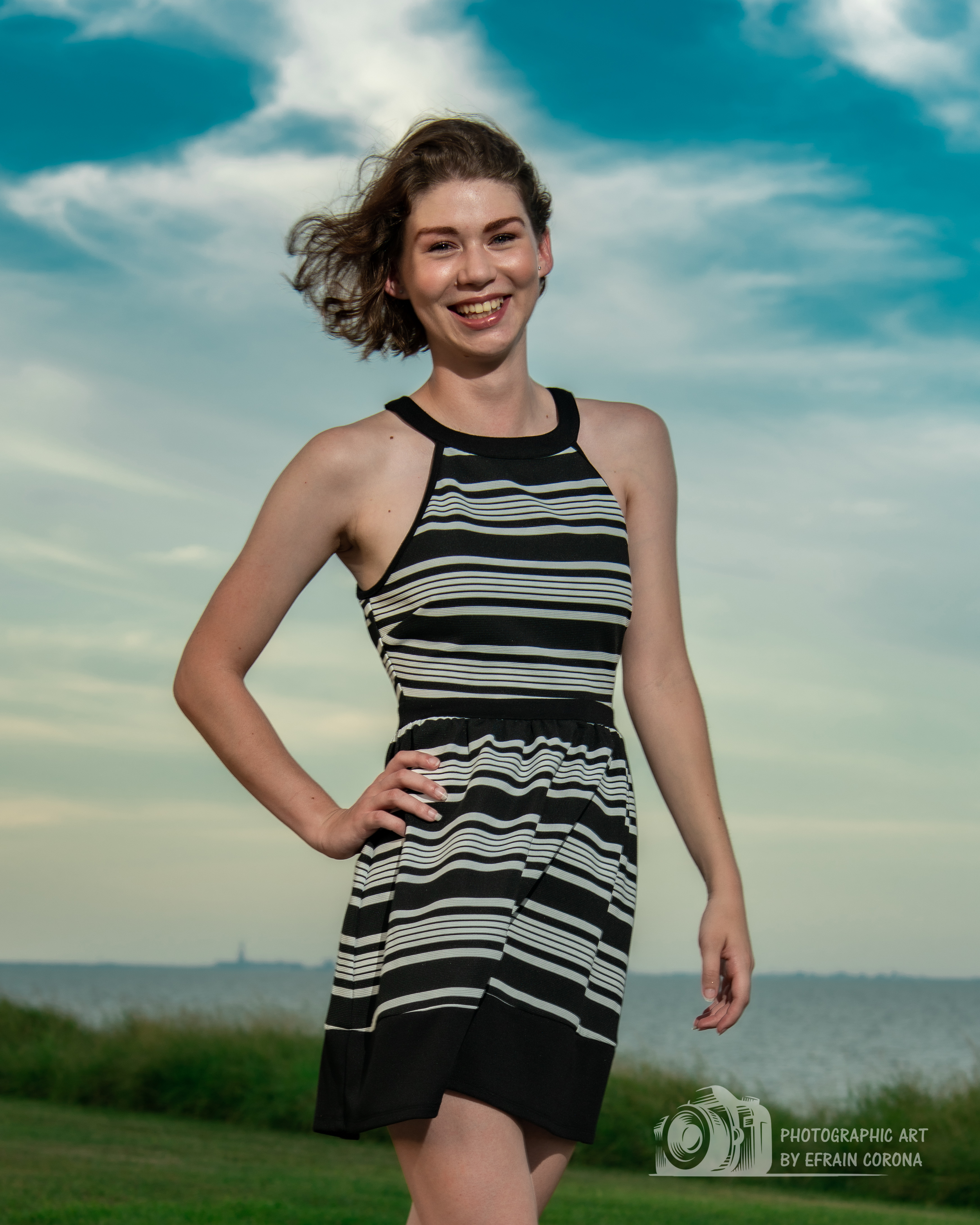 Hailey posing by the ocean in a black and white striped dress.
