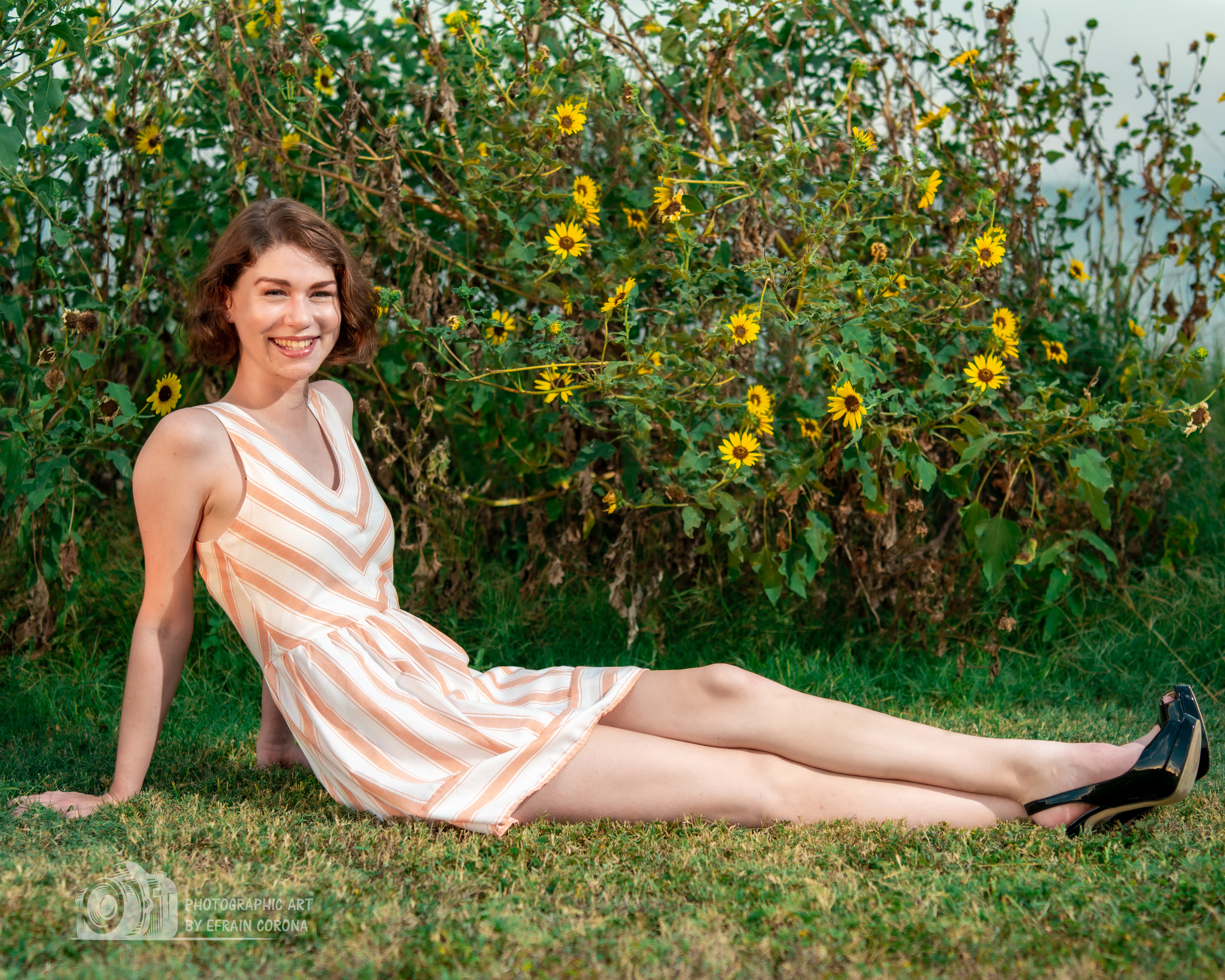 Hailey posing by sunflowers in a peach striped dress.