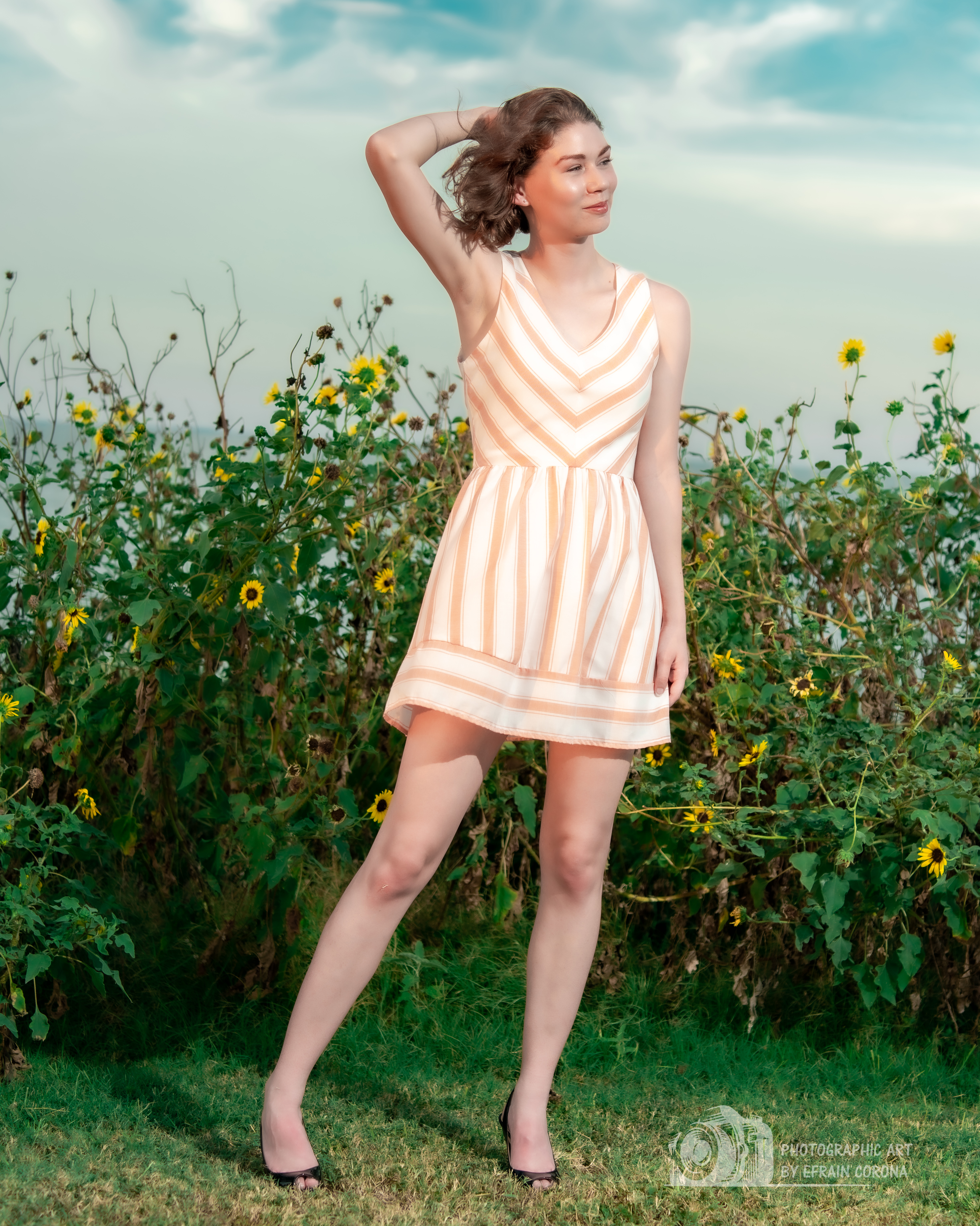 Hailey posing by sunflowers in a peach striped dress.