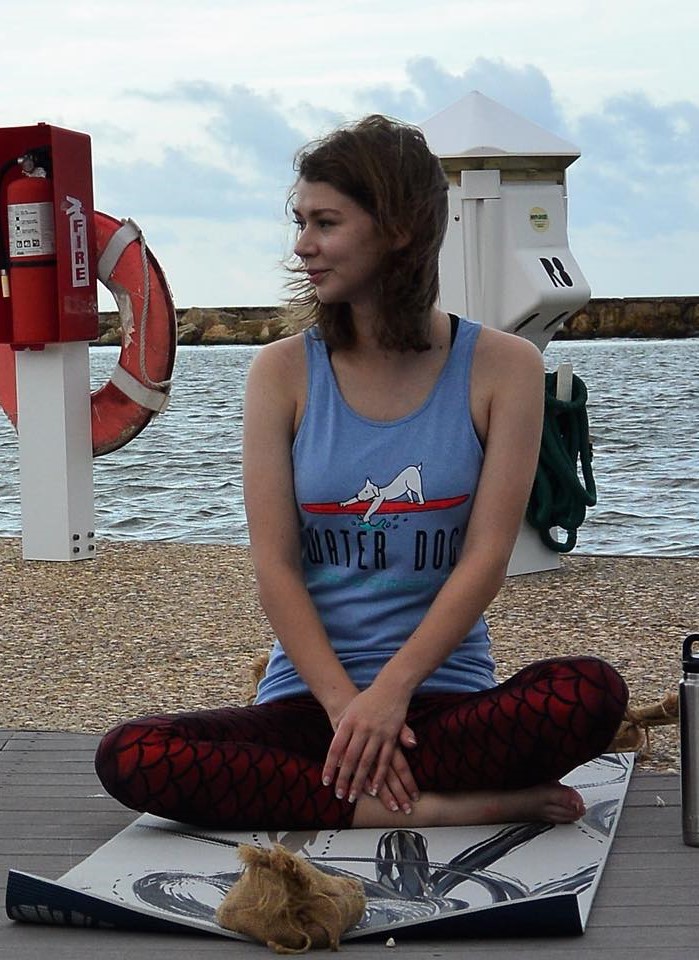 Hailey sitting cross legged on a yoga mat at the marina.